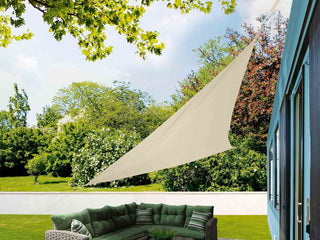 Toldo vela triangular color beige instalado en jardín sobre muebles de exterior